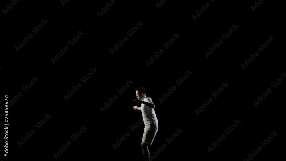 Handsome male gymnast in white clothes on a black background jumping on a trampoline side view Handsome male gymnast in white clothes on a black background jumping on a trampoline side view
