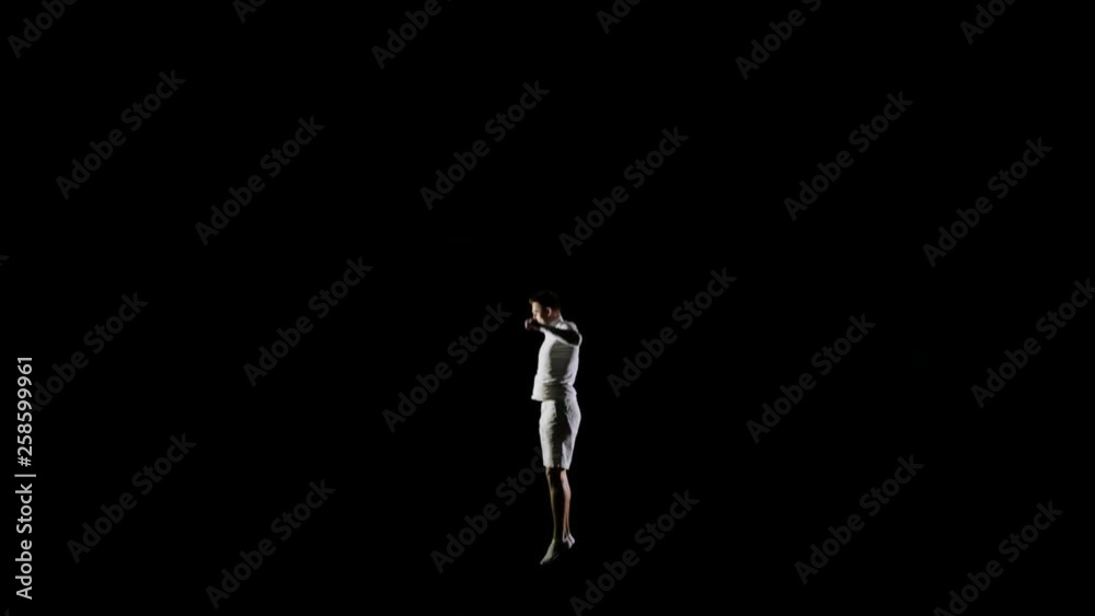 Athletic man in white clothes performs tricks jumping on a trampoline on a black monophonic background Athletic man in white clothes performs tricks jumping on a trampoline on a black monophonic background