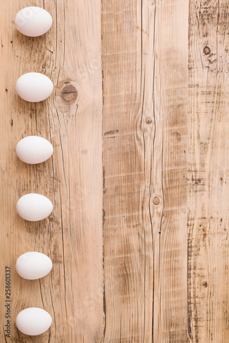 bowl of various fresh eggs on white wooden table, top view