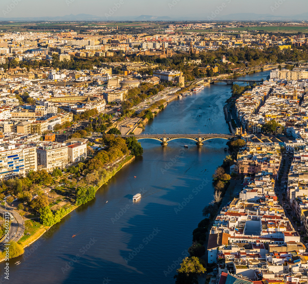 Aerial view of old downtown Sevilla at sunset showing Guadalquivir river, Puente de Triana, Plaza de Toros, Plaza de España, Triana, Torre del Oro, Calle Betis, Parks and other historical buildings.