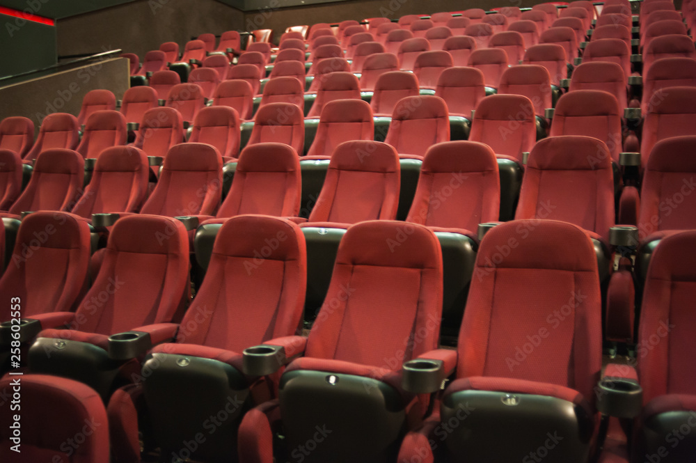 Fototapeta premium Empty cinema. Rows of comfortable red chairs towards to big screen in illuminate red room cinema. Mock Up.