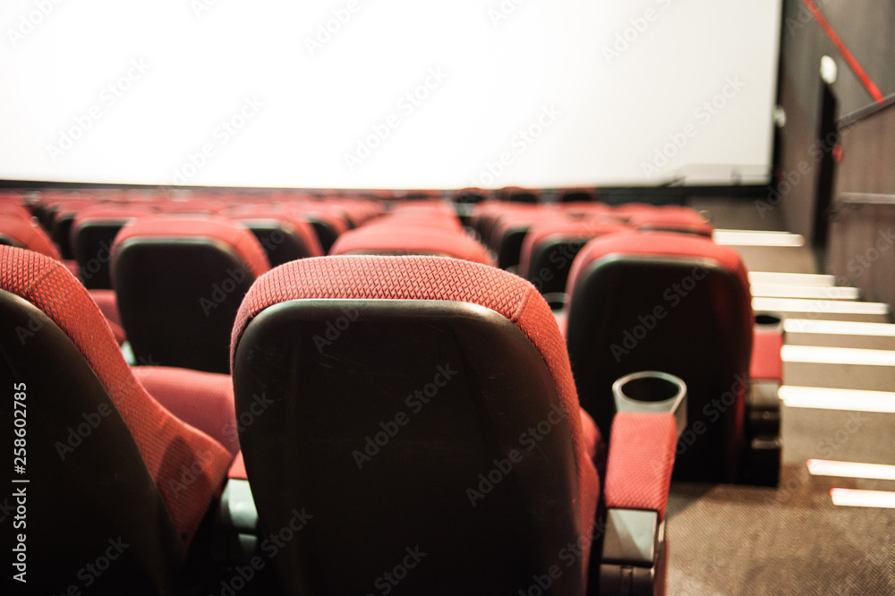 Empty cinema. Rows of comfortable red chairs towards to big screen in illuminate red room cinema. Mock Up.