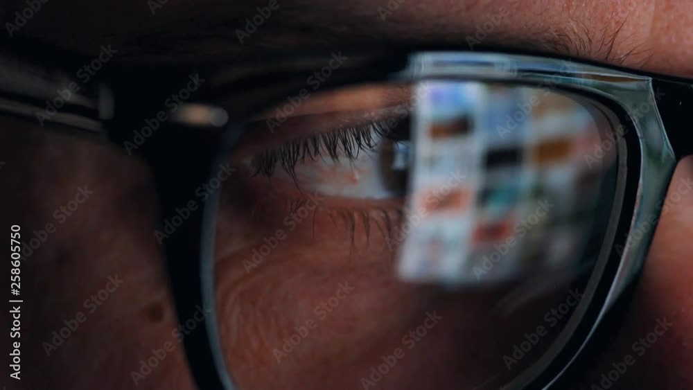 Man in glasses looking on the monitor and surfing Internet. The monitor screen is reflected in the glasses Man in glasses looking on the monitor and surfing Internet. The monitor screen is reflected in the glasses