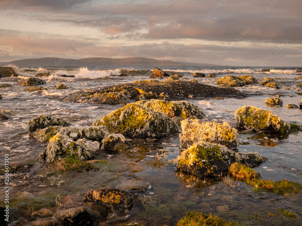 West coast of Ireland, Galway bay shore line, rocks, waves, Burren mountains in the background. Dramatic sky.