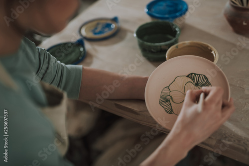 Young lady painting ceramic plate at workshop