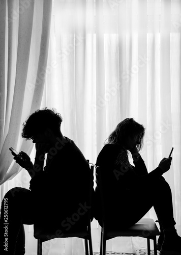 Teenagers sitting back to back looking at their cell phones, black and white effect