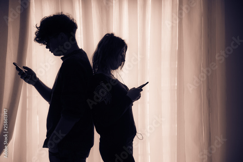 Silhouette of two teenagers with cell phones standing back to back, brown effect