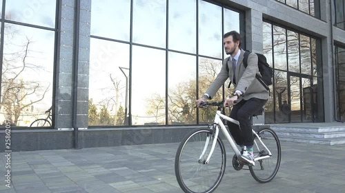 Modern young businessman bicycle rider in suit and with backpack outdoors