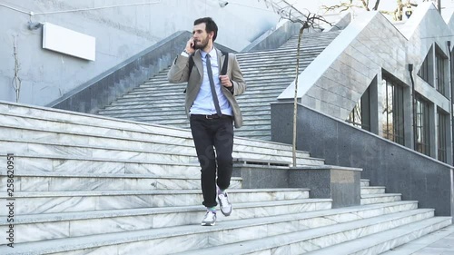 Young male businessman with backpack run on the stairs outdoors and talk with cellphone 
