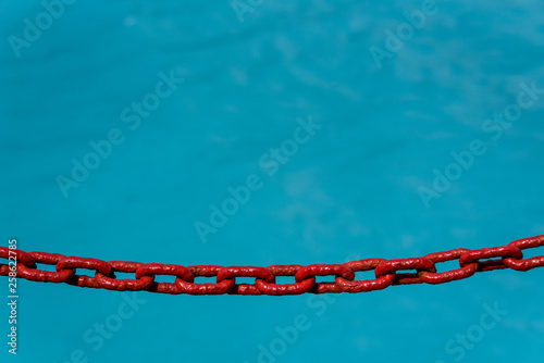 Red painted chain as a barrier to falling into the glacial melt blue ocean, as a background