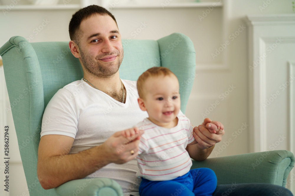 father and his son. daddy's little boy. man holding his baby on laps sitting in living room. father's love, family value, loving relationship father and his son. daddy's little boy. man holding his baby on laps sitting in living room. father's love, family value, loving relationship