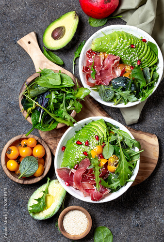 Low carbs bowl. Fresh salad with green spinach, rucola, avocado an ham serrano in white bowl, gray background, top view