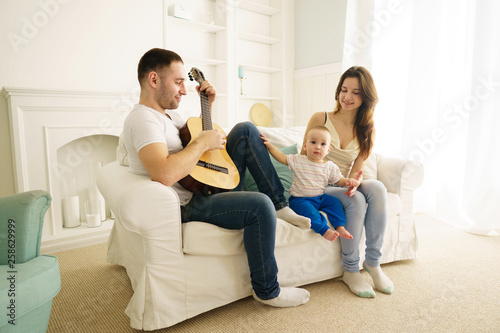 Family weekend, parents with little son in living room. Daddy playing guitar for mom and son. Music, happiness and leisure activities © Vadym