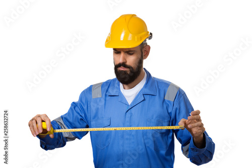 Handsome builder with beard is holding tape-measure in his hands. Isolated on white