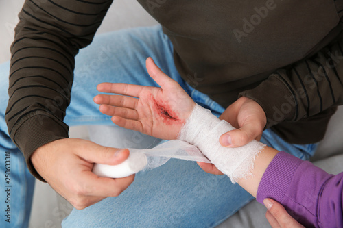 Quadro em tela Young man applying bandage on woman's injured hand at home, closeup