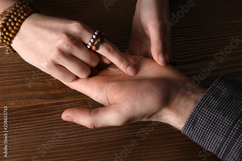 Chiromancer reading lines on man's palm at table, closeup