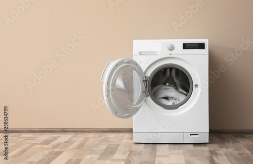 Modern washing machine with laundry near color wall, space for text photo