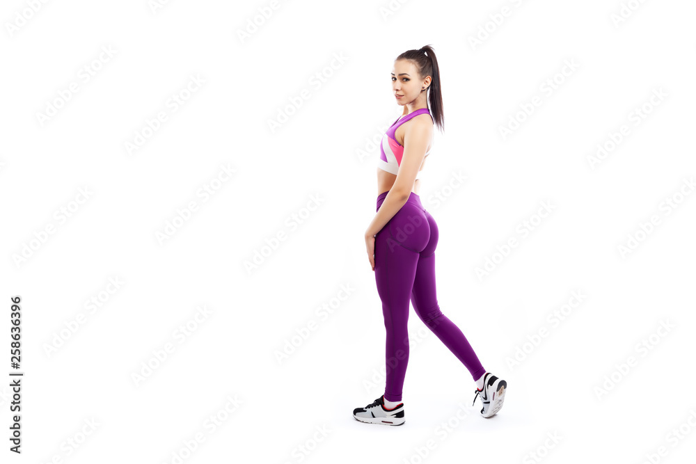 A young woman coach in a sporty pink short top and gym leggings posing, doing exercise, step forward on a white isolated background in studio A young woman coach in a sporty pink short top and gym leggings posing, doing exercise, step forward on a white isolated background in studio