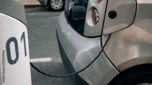 Detail - an electrocar with a charging cord, connecting it to a charger photo