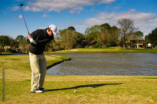 Golfer taking practice swings on the tee box with ball and hole in the frame