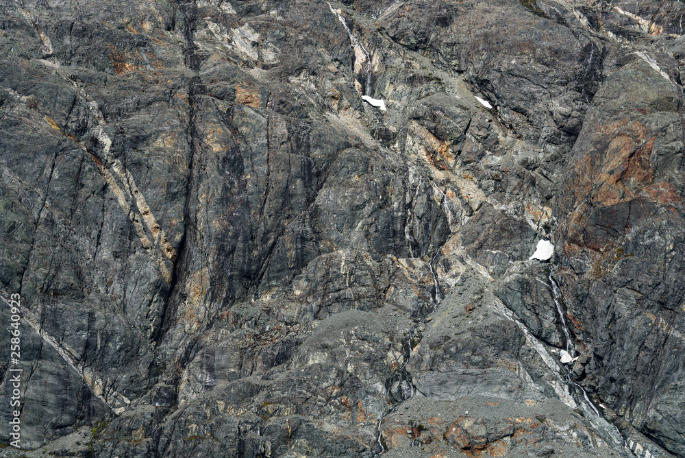 Weathered gray rock face with orange and white mineral veins as a nature background Weathered gray rock face with orange and white mineral veins as a nature background