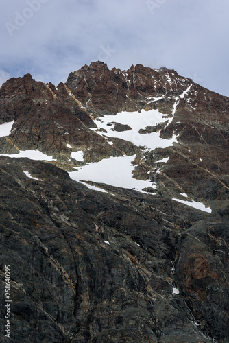 Beautiful rocky mountain peaks with veins of orange minerals, snow patches, and blue sky with wispy white clouds