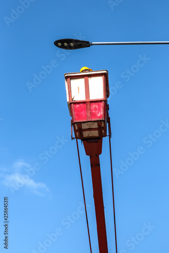 Technician on bucket truck high up of a crane to fix street light.