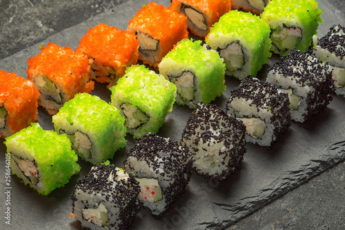 Set of assorted japanese sushi food on a black stone plate, close up angle view. Rolls with tuna, salmon, shrimp, crab and avocado. Sushi menu.