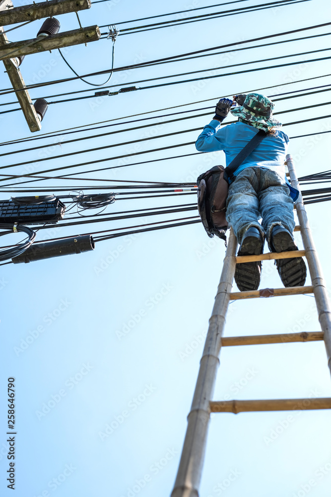 Electrician climbing the bamboo ladder to repair electric wires.