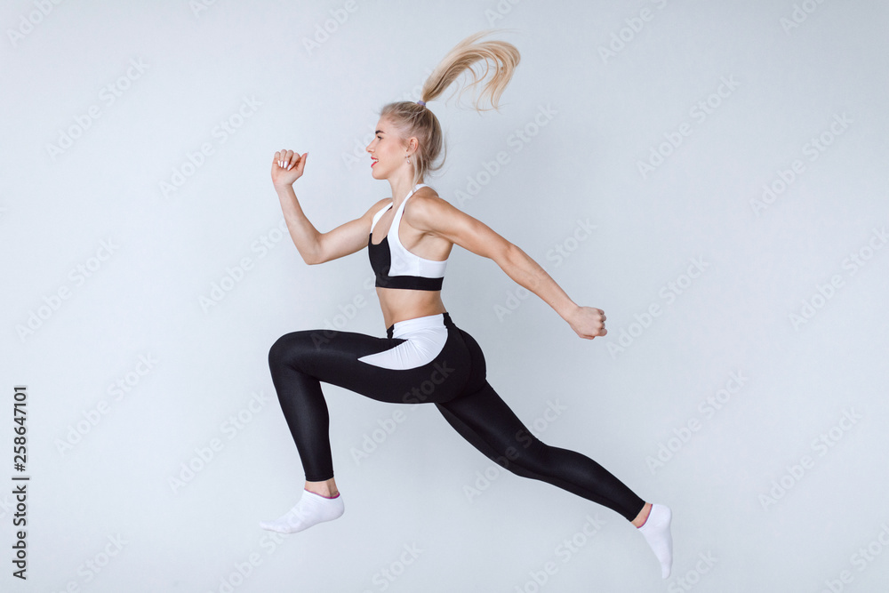 Sporty woman runner  in black and white sportswear on grey background. Dynamic movement.
