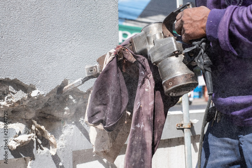 Worker demolish concrete wall using jackhammer.