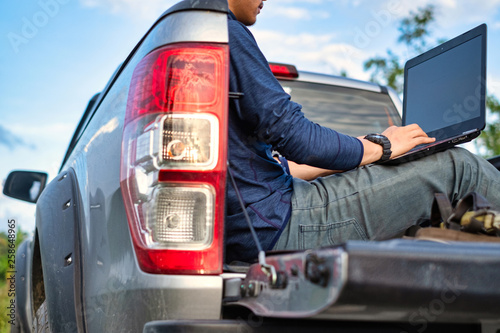 Young Asian field worker with tools sitting on pickup trunk. Working in field. photo