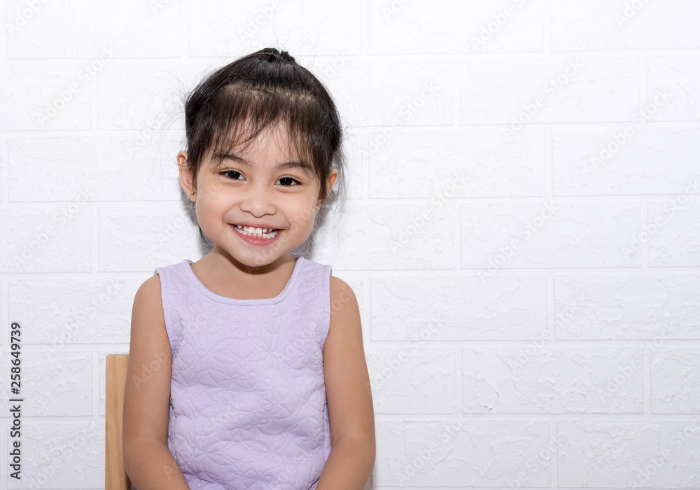 Female asian child girl sitting on a chair with white background smiling