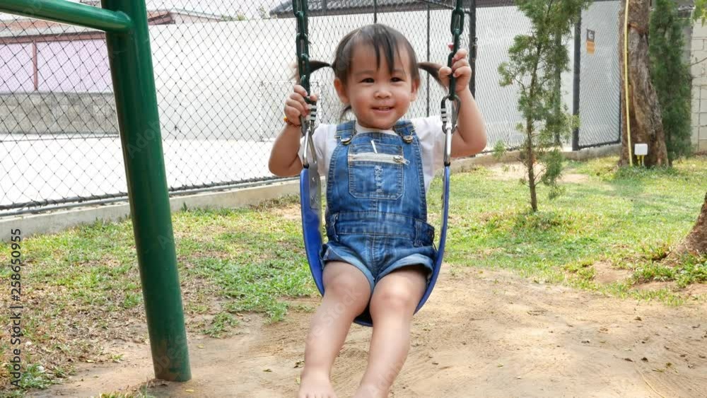 Asian little child is sitting on a swing happily at the playground. Asian little child is sitting on a swing happily at the playground.