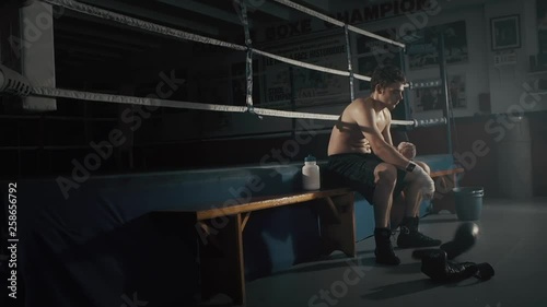 Cinematic shot of the young boxer sitting on the bench after the training.