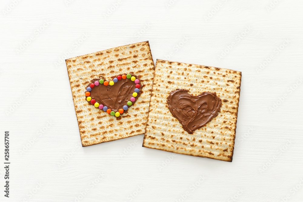 Pesah celebration concept (jewish Passover holiday) with chocolate heart and colorful candies over matzah. Top view flat lay