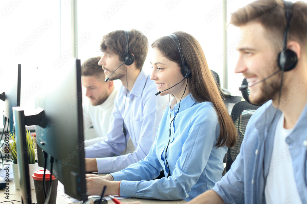 Fototapeta premium Portrait of call center worker accompanied by her team. Smiling customer support operator at work.