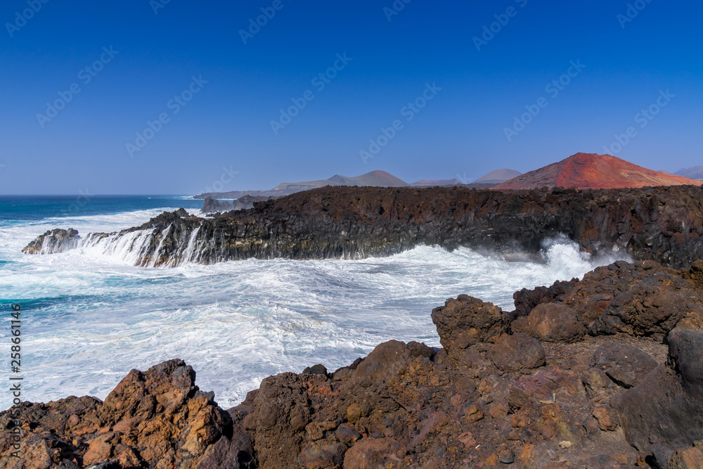 Spain, Lanzarote, Rough atlantic sea in los hervideros cove next to red volcanoes