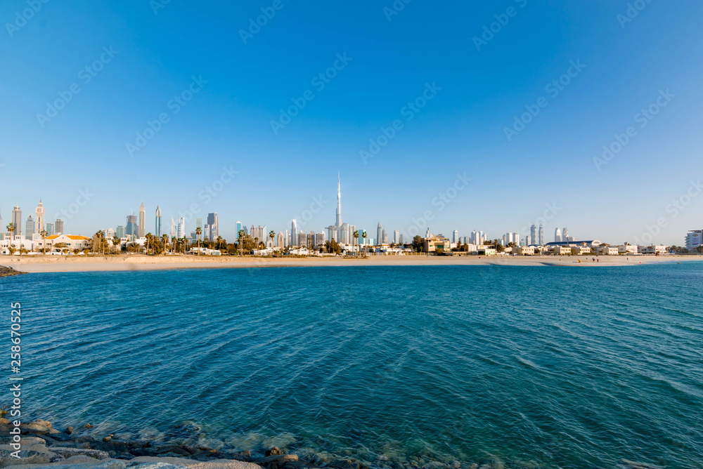 Futuristic Skyscraper buildings view from rock beach island with blue waterfront and  blue sky background