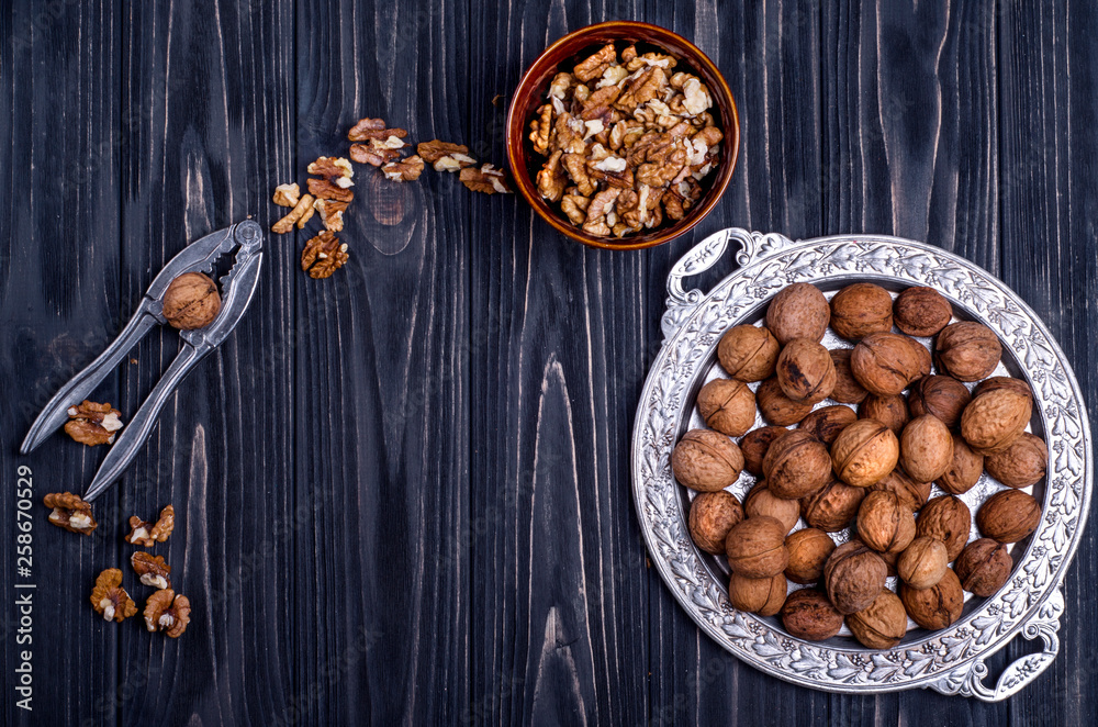 Fototapeta premium Walnuts and walnut kernelsin a silver dish on a dark wooden background