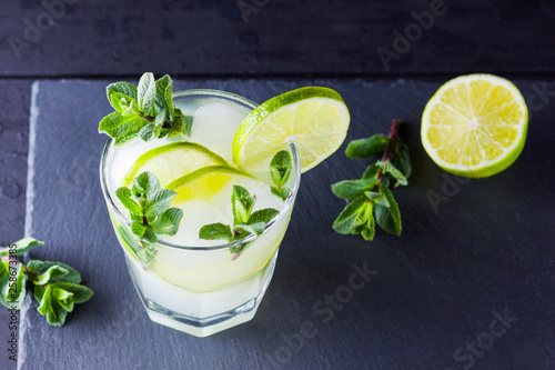 Cocktail mojito and mint on black background. Refreshing cocktail with lime and fresh mint on slate board. Summer drink with citrus and ice