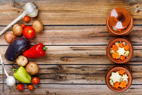 Traditional rustic home vegetable stew with raw vegetables and spices in clay pots on an old vintage wooden table.