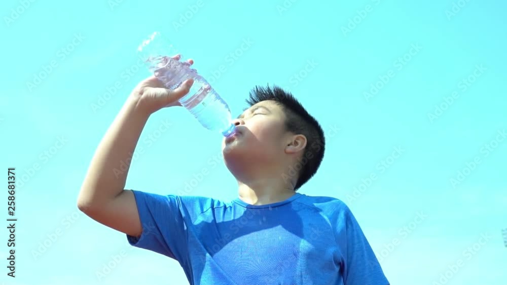 Slow motion young Asian boy drink water from a bottle under blue sky