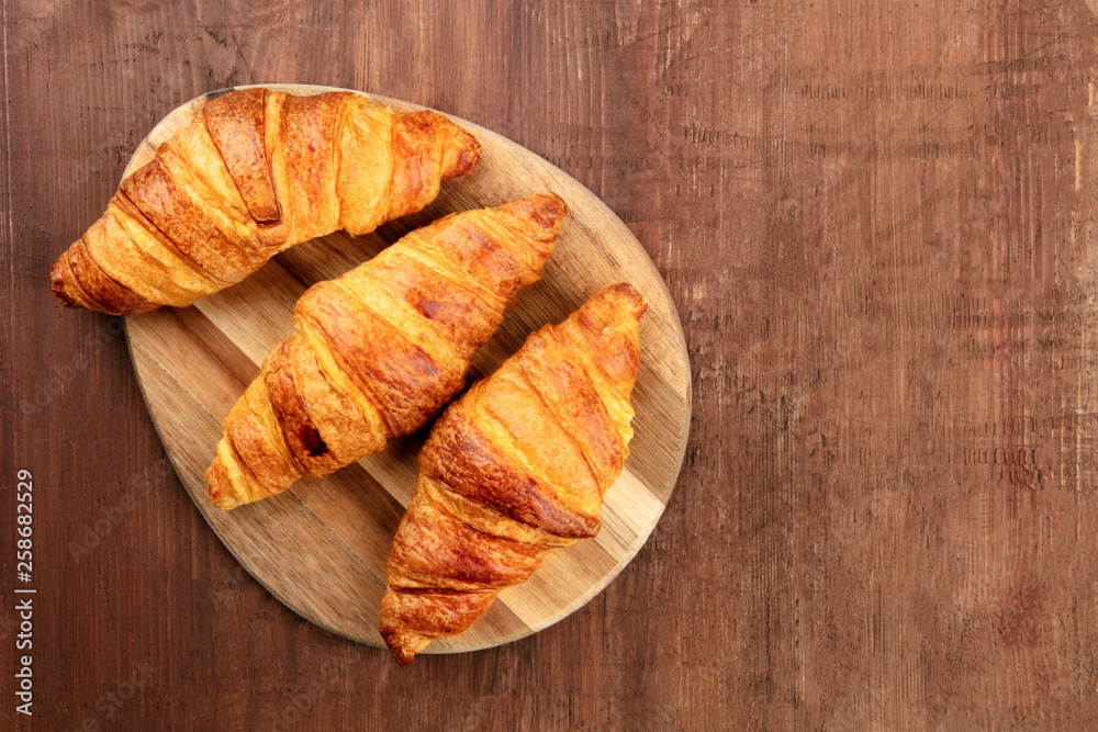 Three croissants, shot from above on a dark rustic wooden background with a place for text