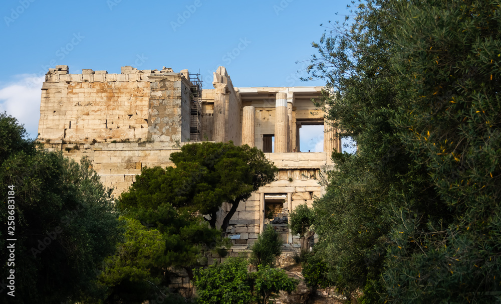 View of Propylaea entrance to Acropolis area on Athens, Greece against clear blue sky and greenery View of Propylaea entrance to Acropolis area on Athens, Greece against clear blue sky and greenery