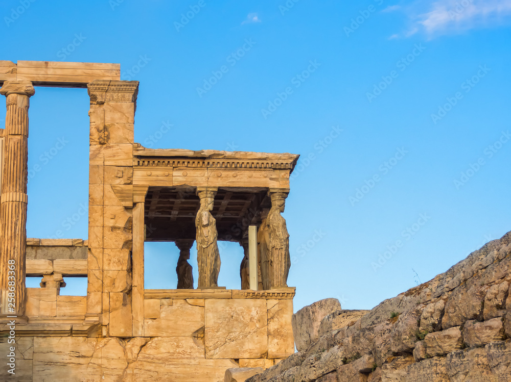 Porch of Poseidon, part of Erechtheion, sacred olive tree, walls of temple of Athena Polias on Acropolis, Athens, Greece against blue sky