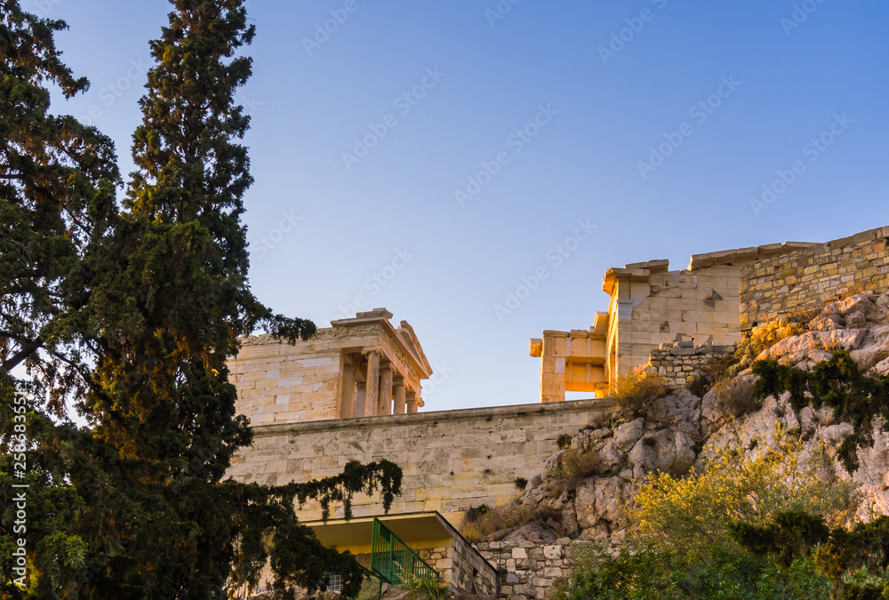 View from below and aside of temple of Athena Nike and Propylaea entrance gateway on Acropolis, Athens, Greece against blue sky