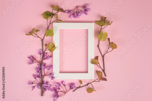 Flowers composition. Purple flowers, leaves and photo frame on pastel pink background. Flat lay, top view, copy space