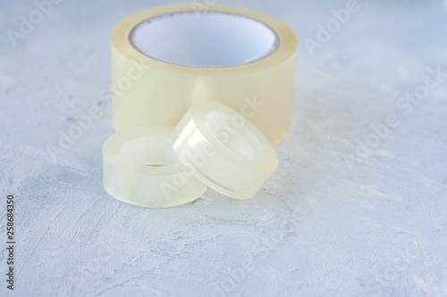 Set of glue packing tape with selective focus on grey cement background. Repair plastic tapes on neutral surface. Bobbin with transparent sticky sellotape. Fix or packaging tapes