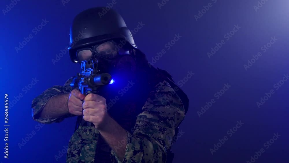 Soldier in gas mask turns around and points assault rifle in blue smoke